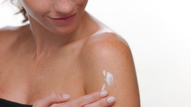 Beauty woman with freckles applies body cream on shoulder