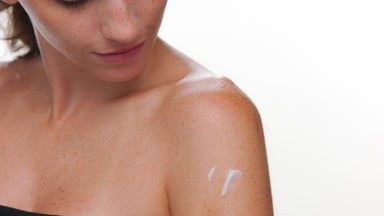 Freckled fair-skinned model applies cream on shoulder white bg