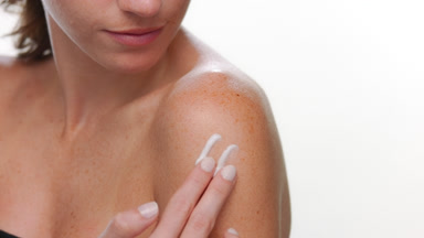 Brunette latina with freckles applies cream on shoulder light bg