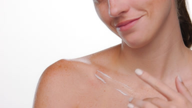 Freckled spanish woman applies moisturizing cream on clavicle