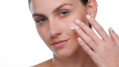 Young adult woman with blue eyes applies face cream on cheek