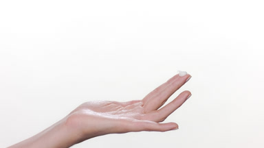Fair-skinned hand with drop of cream on finger white background