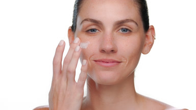 Beauty model with blue eyes applies collagen cream on cheek