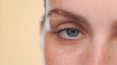 Young light-skinned latina opening her eye on beige background