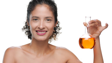 Young latina with curly hair holds orange liquid flask smiles