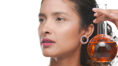 Brown-eyed young woman holds round flask with orange liquid face