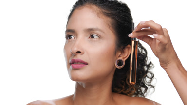Curly-haired beauty move orange test tube along face looks aside