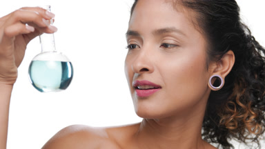 Young latin beauty shows small round blue flask looks at camera