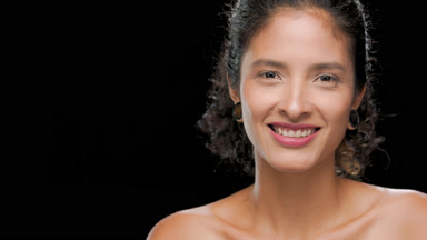 Latin woman with dark curls smiles turns to camera black bg