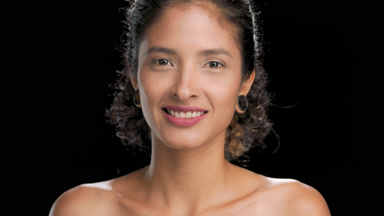 Black-haired hispanic beauty smiles turns to camera dark bg