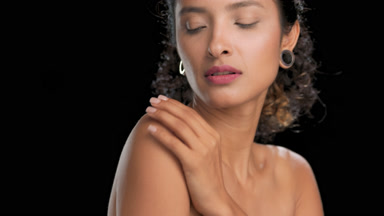 Latin woman with curly hair strokes shoulder looks at camera