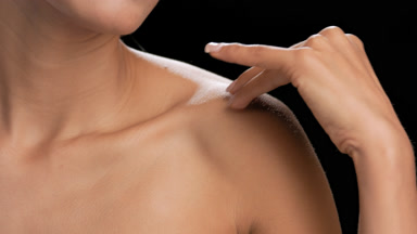 Light brown-skinned woman gently strokes clavicles black bg
