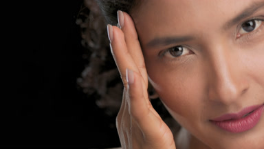 Natural latin model slides hand from cheek to temple dark bg