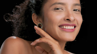 Cheerful latin model with curls strokes jawline smiles black bg