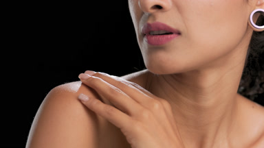 Light brown-skinned woman strokes shoulder skin on black bg