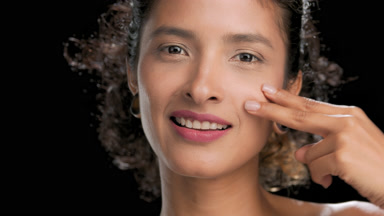 Latin american model strokes under-eye area with fingers on dark