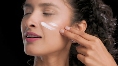 Attractive latin woman applies white face cream on cheek