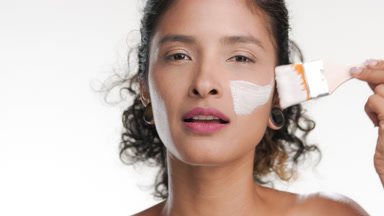 Black-haired hispanic woman applies white clay mask with brush