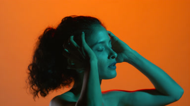 Curly-haired latina with teal light runs fingers through hair