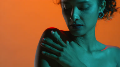 Attractive latin woman lit with teal touches shoulder on orange