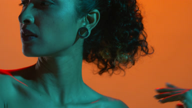 Stylish hispanic woman lit with cyan touches clavicles on orange
