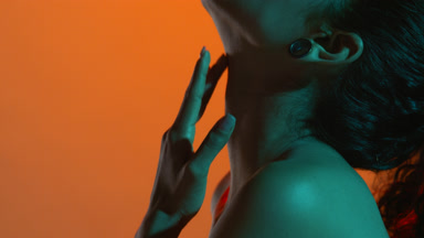 Hispanic woman with cyan gel light touches throat in profile