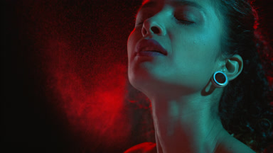 Elegant hispanic woman sprays red mist inhales fragrance on dark