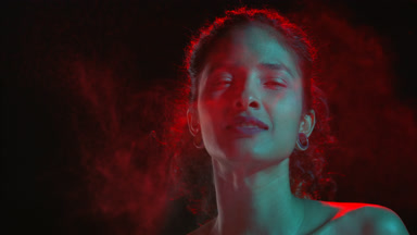 Cheerful latin model in cyan-red light sprays fragrance on black