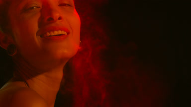 Latin american woman in red-orange light mists air on black