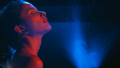 Gorgeous latin woman in blue-red light sprays blue mist on black