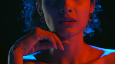 Latin model in blue-red light strokes chin and jawline on black