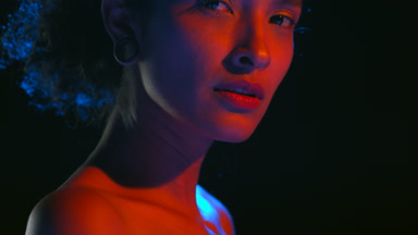 Off-shoulder hispanic woman in blue-red light looks at camera