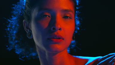 Cheerful latin model in blue-red light strokes skin on black bg