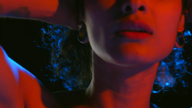 Latin model in red-blue light holds hair with hands on black