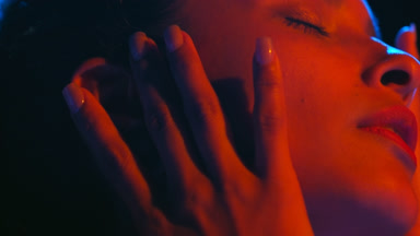 Latin woman under red blue gel lights touches face eyes closed