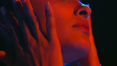 Hispanic beauty with red and blue light touches face eyes closed