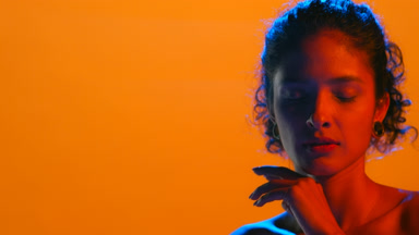 Latin woman with curly hair in red and blue light touches chin
