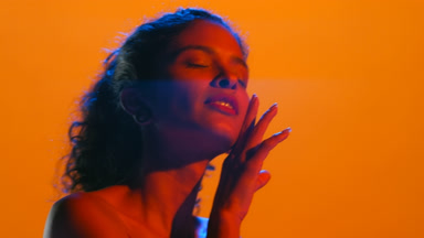 Beautiful latin woman in blue and red led touches chin looks up