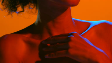 Young woman in red and blue light strokes shoulder to clavicles