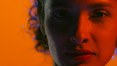 Latin woman in blue and red gel light turns face to camera