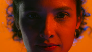 Latin woman with curls in red light opens eyes looks at camera