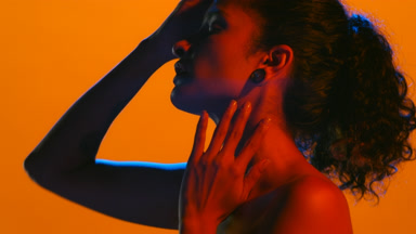Woman in blue and red light turns profile touches face and hair