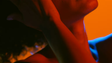 Cheerful latin woman in red and blue gel light touches face hair