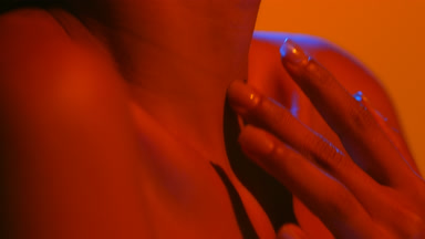 Woman in blue-red light strokes throat neck on orange bg