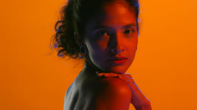 Latin beauty in red light hand on shoulder orange bg