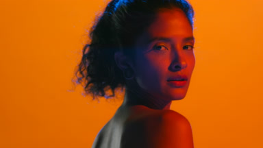 Latin model in red led looks over shoulder orange bg
