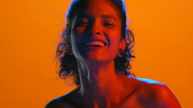 Hispanic woman laughs in red-blue light orange background