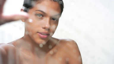 Skin care model wipes moist from wet glass surface