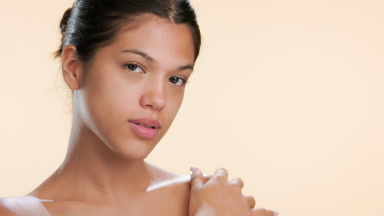Young beauty strokes shoulder looks at camera moisturized skin