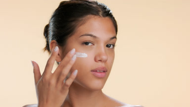 Beauty model applies cream on cheek with her finger